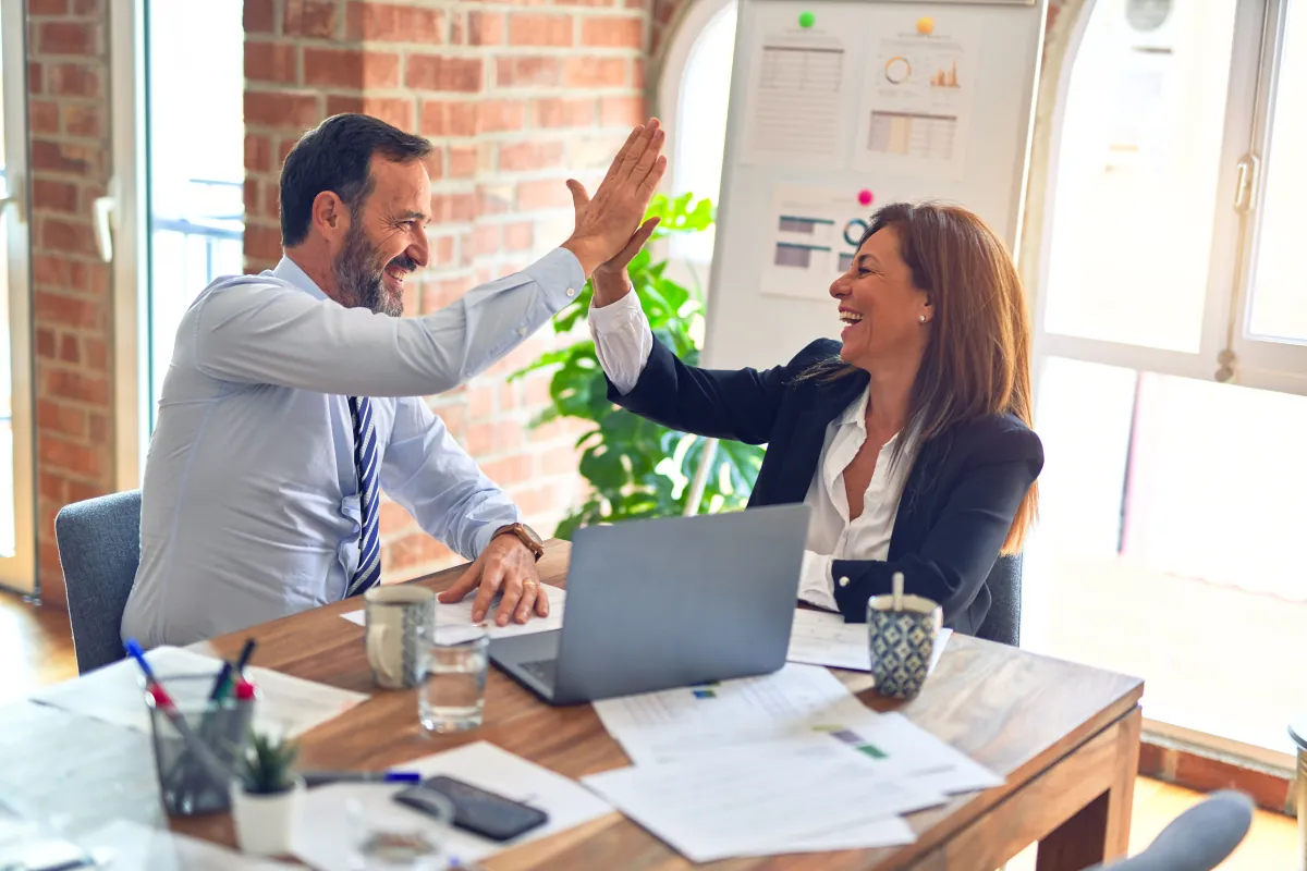 Two business partners celebrating with a high five at their desk